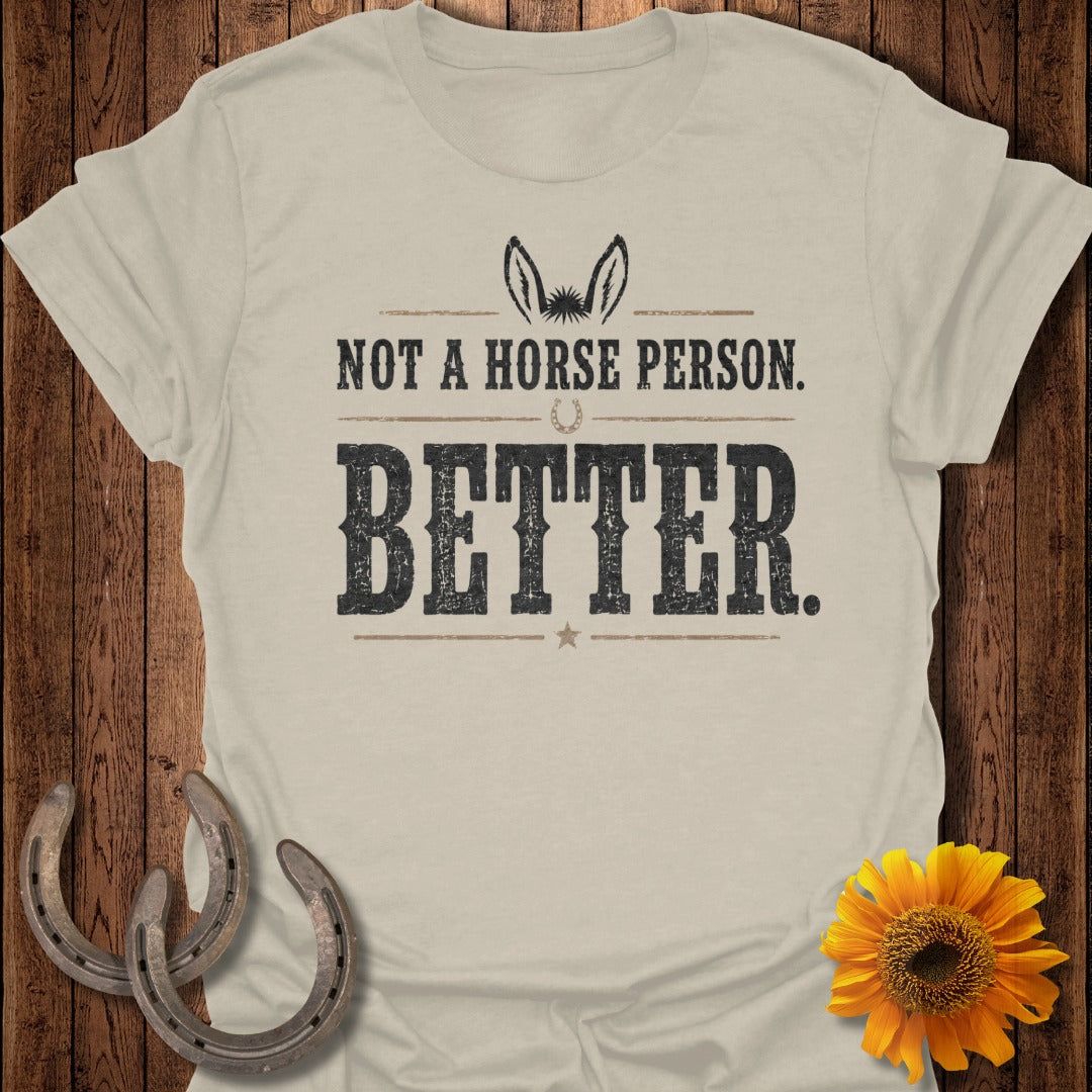 Light beige t-shirt with text "NOT A HORSE PERSON. BETTER." and donkey ears decor.