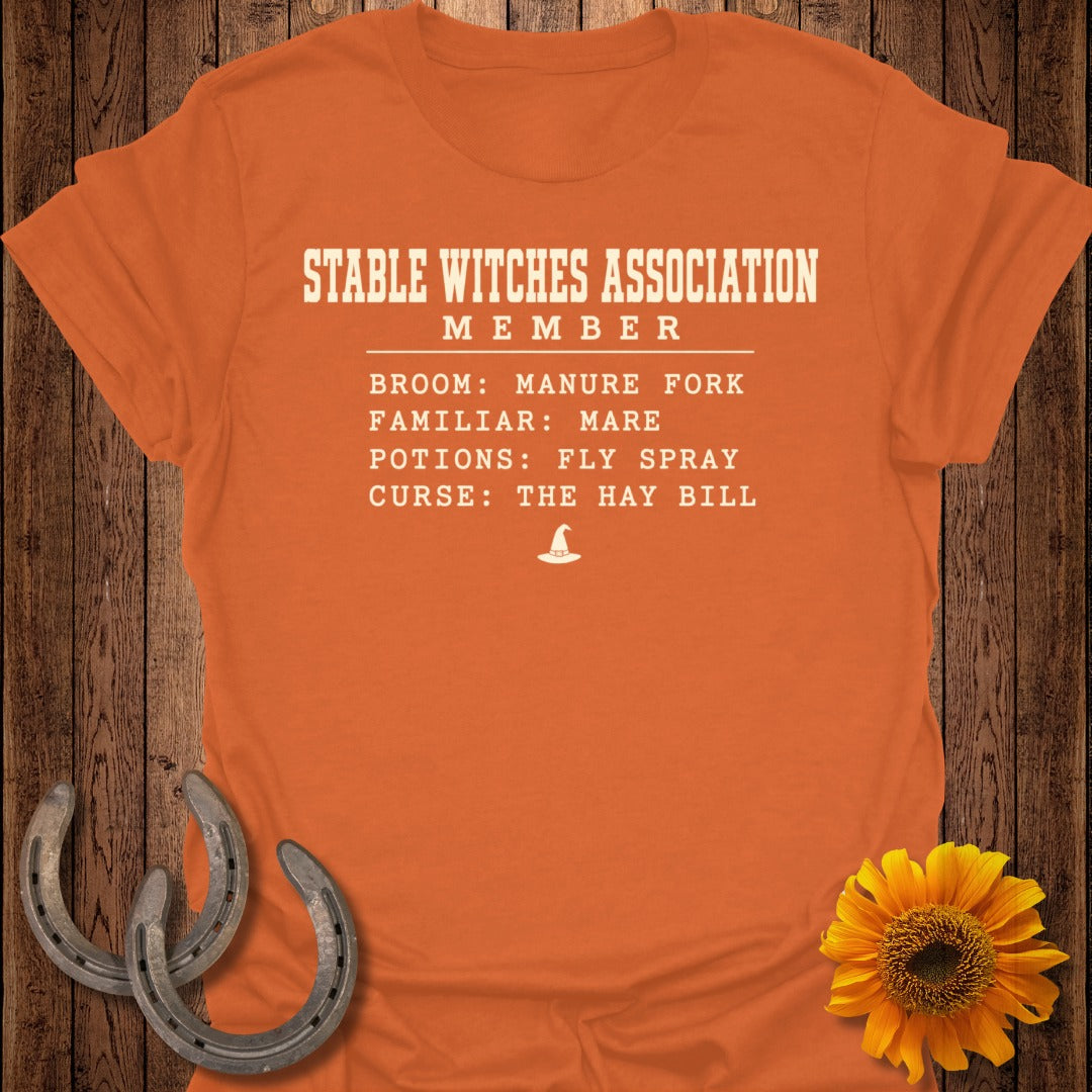 Orange t-shirt with "Stable Witches Association Member" text and witch hat graphic.