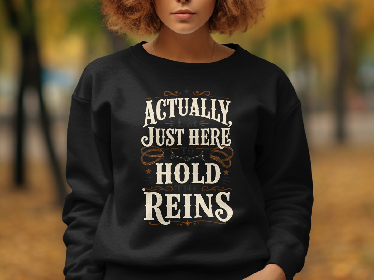 Black sweatshirt with text "Actually, I'm Just Here To Hold The Reins" and horse tack graphic.