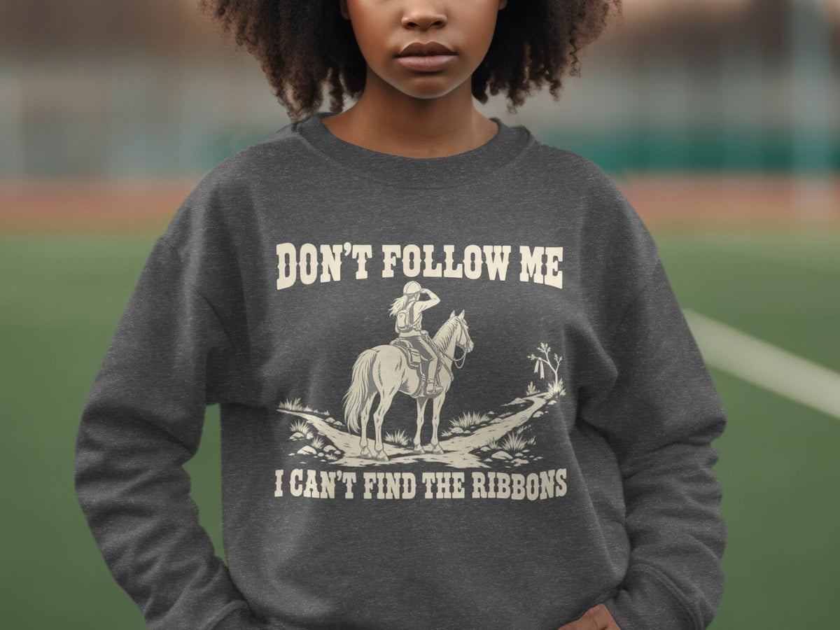 A dark gray crewneck sweatshirt featuring a graphic of a horse rider and the text DON'T FOLLOW ME I CAN'T FIND THE RIBBONS.