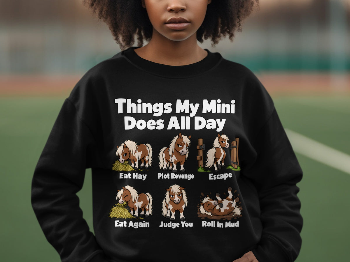 A person wearing a black sweatshirt printed with mini horse illustrations and humorous captions.