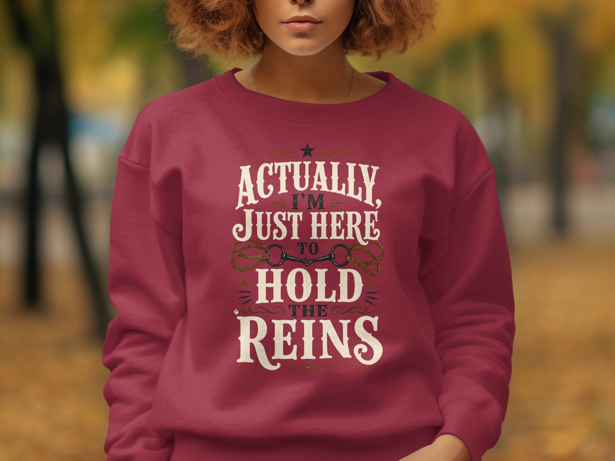 Maroon sweatshirt with "Actually I'm Just Here to Hold the Reins" text.