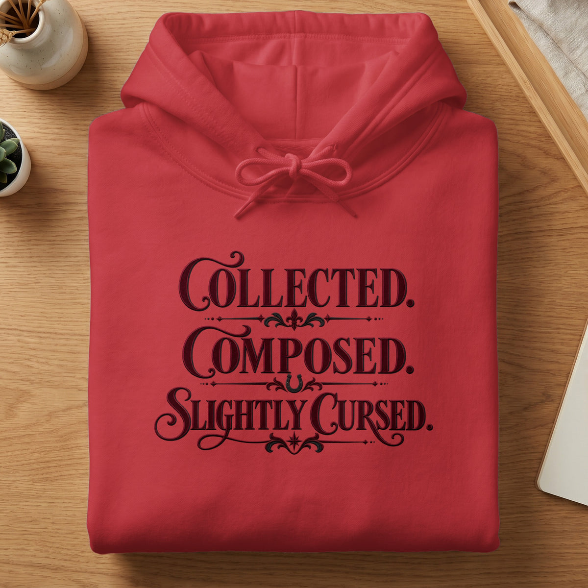 Red hoodie with "Collected. Composed. Slightly Cursed." text in dark lettering.