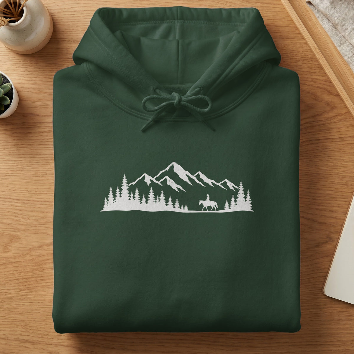 Dark green hoodie with white mountain, forest, and equestrian silhouette graphic.