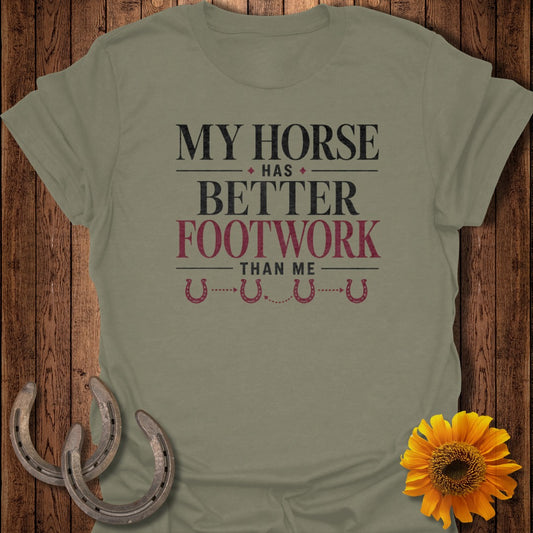 Olive green t-shirt with text "MY HORSE HAS BETTER FOOTWORK THAN ME" and horseshoes.