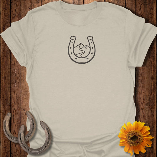 Light tan t-shirt with horseshoe and mountain logo, two horseshoes, and sunflower.