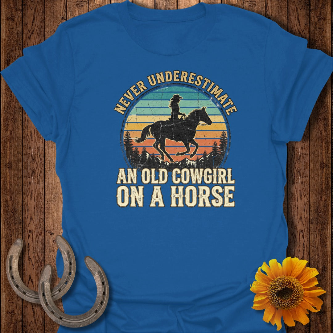 Blue t-shirt with distressed vintage sunset and "Never Underestimate An Old Cowgirl On A Horse" text.