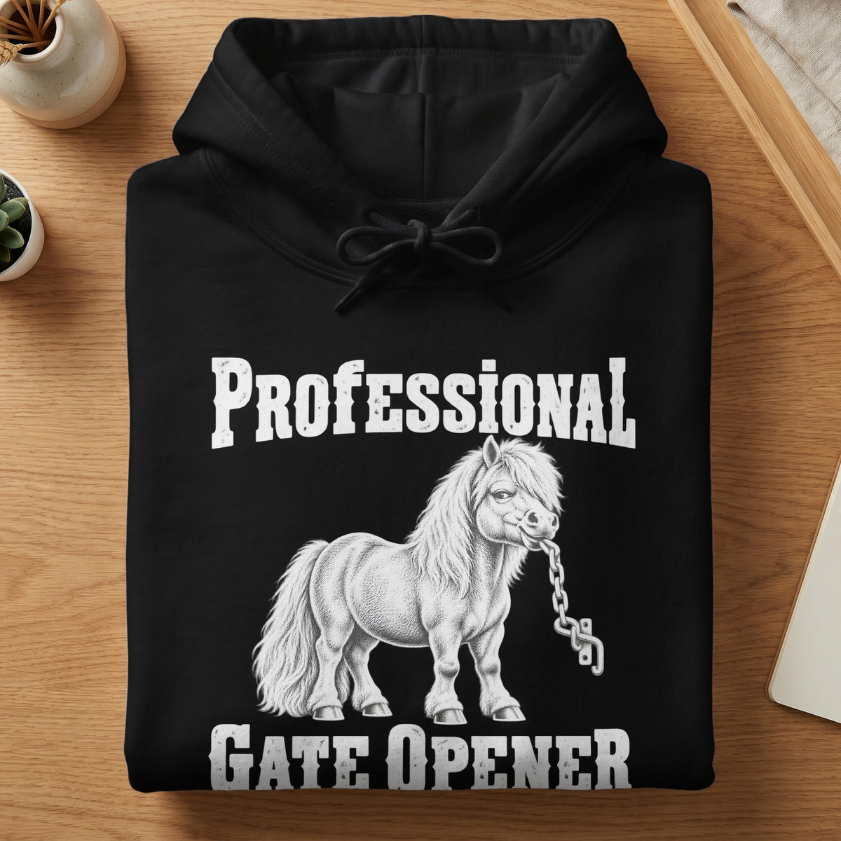A folded black hoodie features white text reading Professional Gate Opener with a pony chewing a chain.