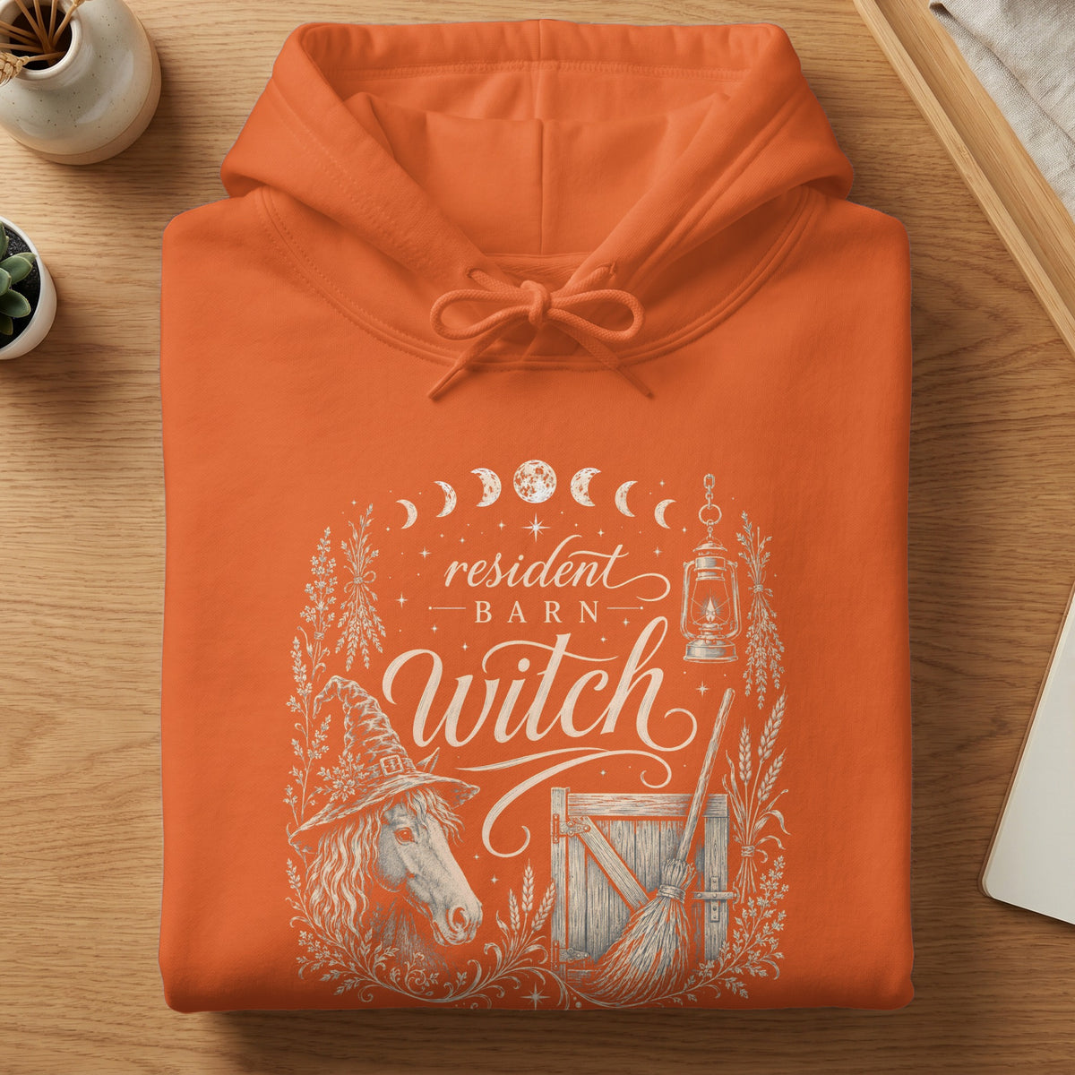 Orange hoodie with "Resident Barn Witch" design featuring a horse, broom, and lantern.