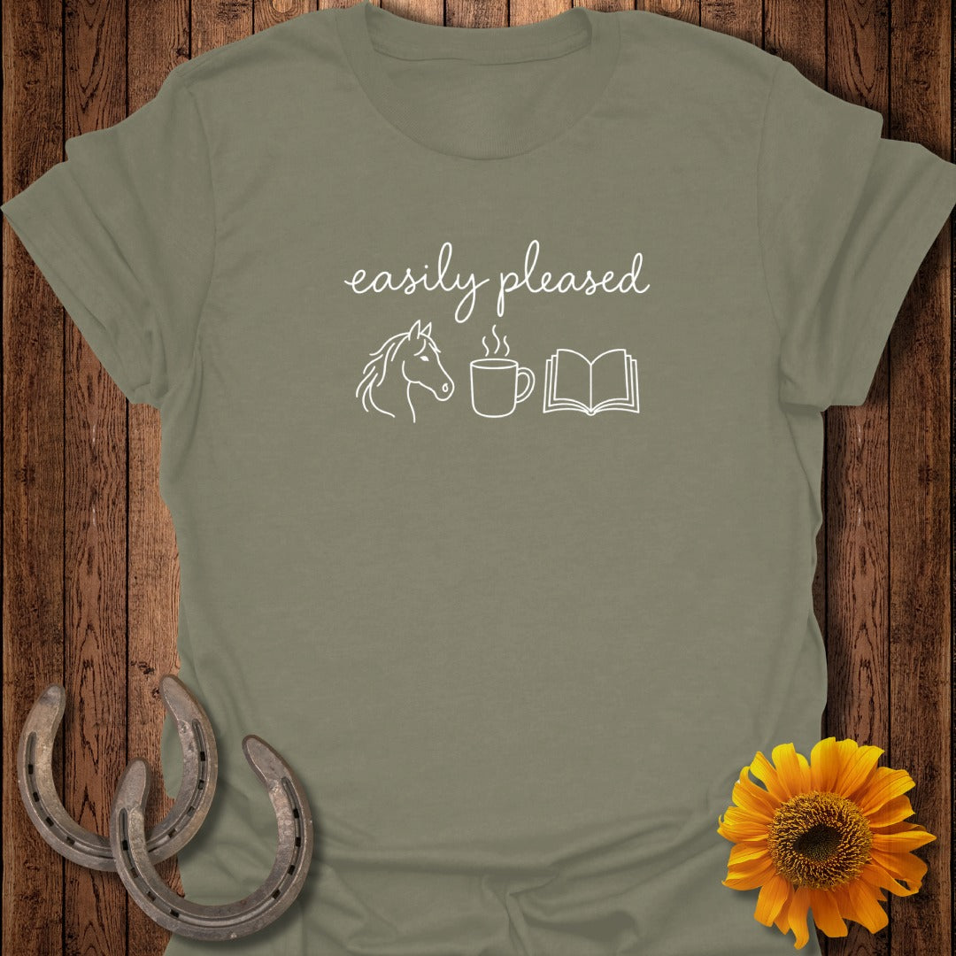Olive green t-shirt featuring white text that reads easily pleased above line drawings of a horse, coffee cup, and open book.