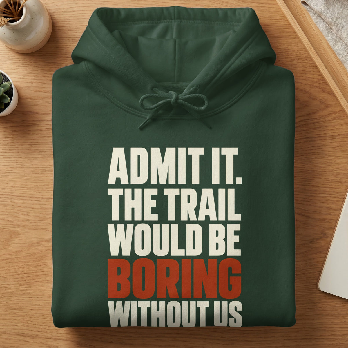 A folded dark green hooded sweatshirt with white and orange text reading Admit It. The Trail Would Be Boring Without Us.