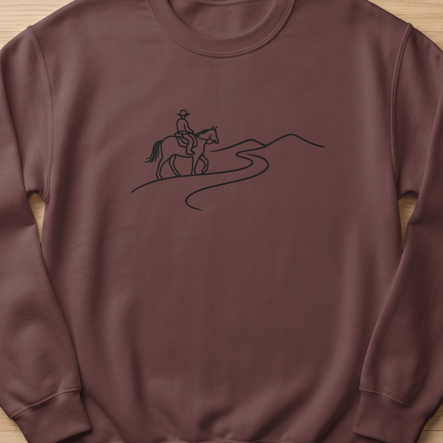 Brown sweatshirt with a black line drawing of a person on horseback on a winding path.