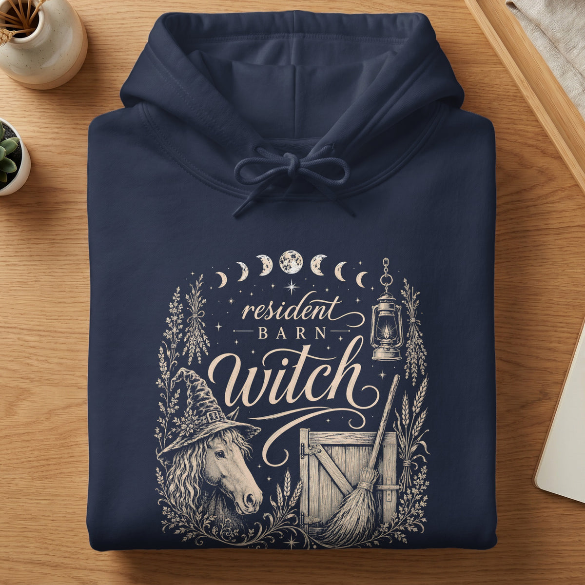 Dark navy hoodie with "resident barn witch" design featuring horse, lantern, and broom.