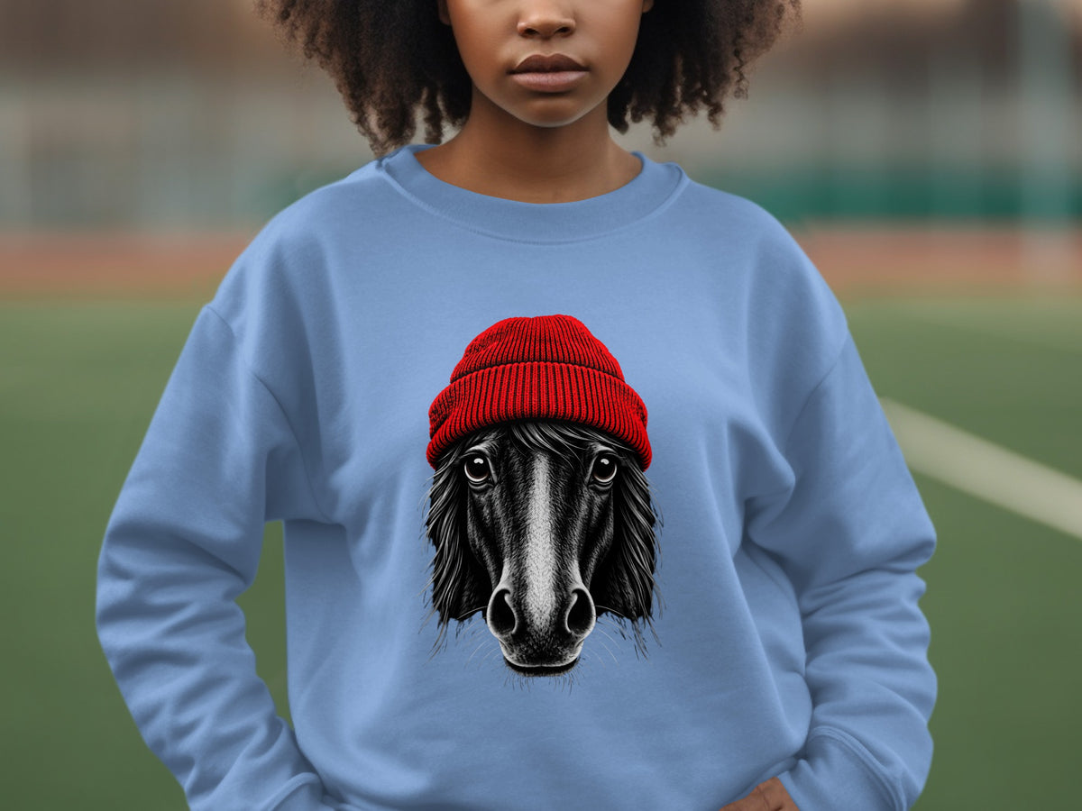 A person wearing a light blue sweatshirt printed with a black and white horse wearing a red beanie.