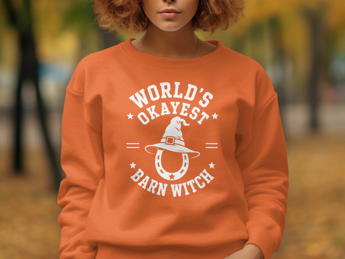 Orange sweatshirt with "World's Okayest Barn Witch" text and horseshoe with witch hat graphic.
