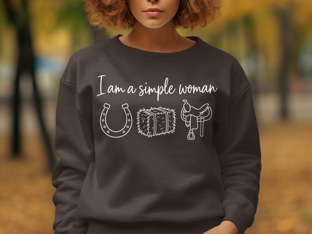 Dark brown sweatshirt with white text and graphics: "I am a simple woman" above horseshoe, hay bale, and saddle.