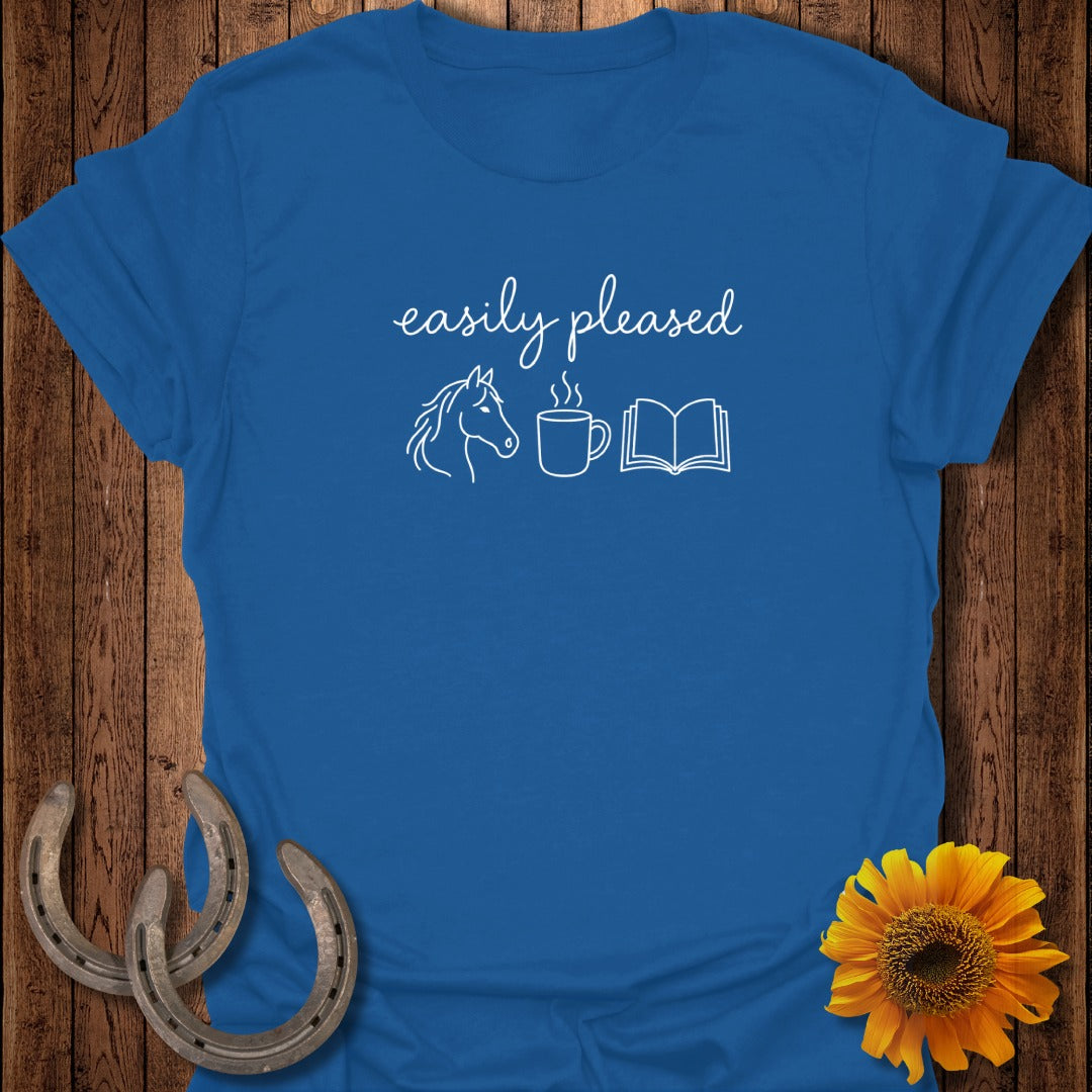 A royal blue t-shirt printed with the white text "easily pleased" above a horse, a steaming coffee mug, and an open book.
