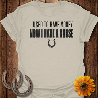 Light tan t-shirt with black text "I USED TO HAVE MONEY NOW I HAVE A HORSE" and horseshoe graphic.