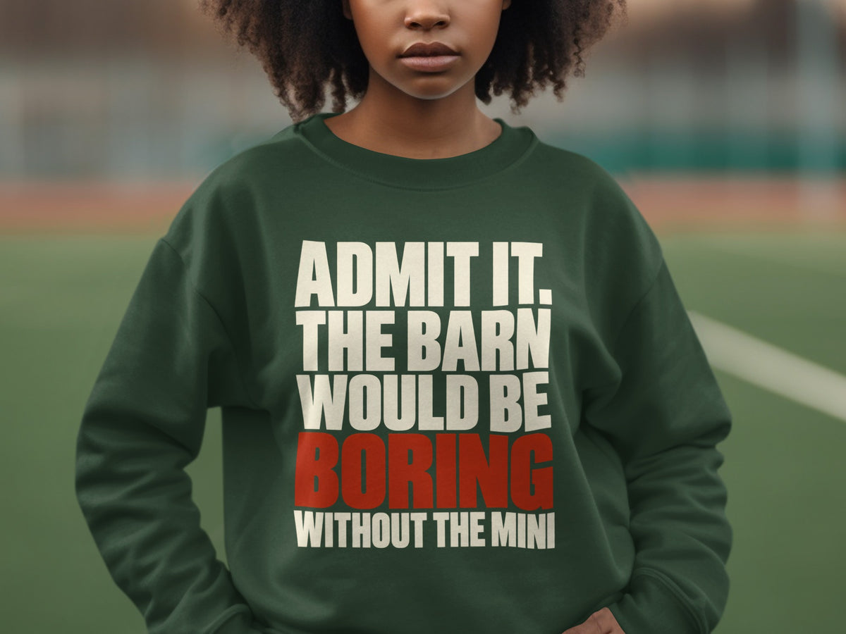 A person wearing a dark green crewneck sweatshirt featuring white and red text stating, ADMIT IT, THE BARN WOULD BE BORING WITHOUT THE MINI.