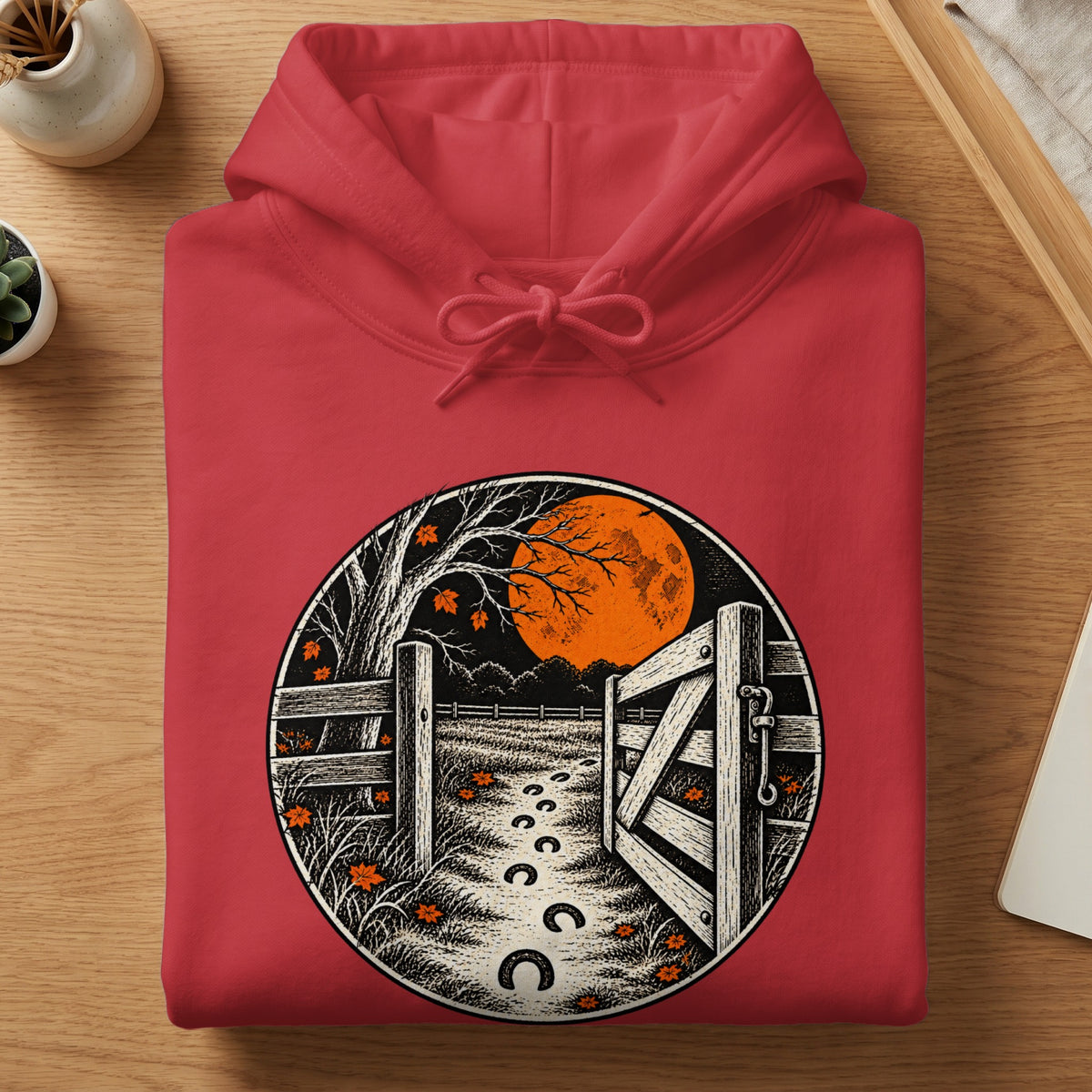 Red hoodie with a circular graphic of a moonlit farm scene and horseshoe prints.