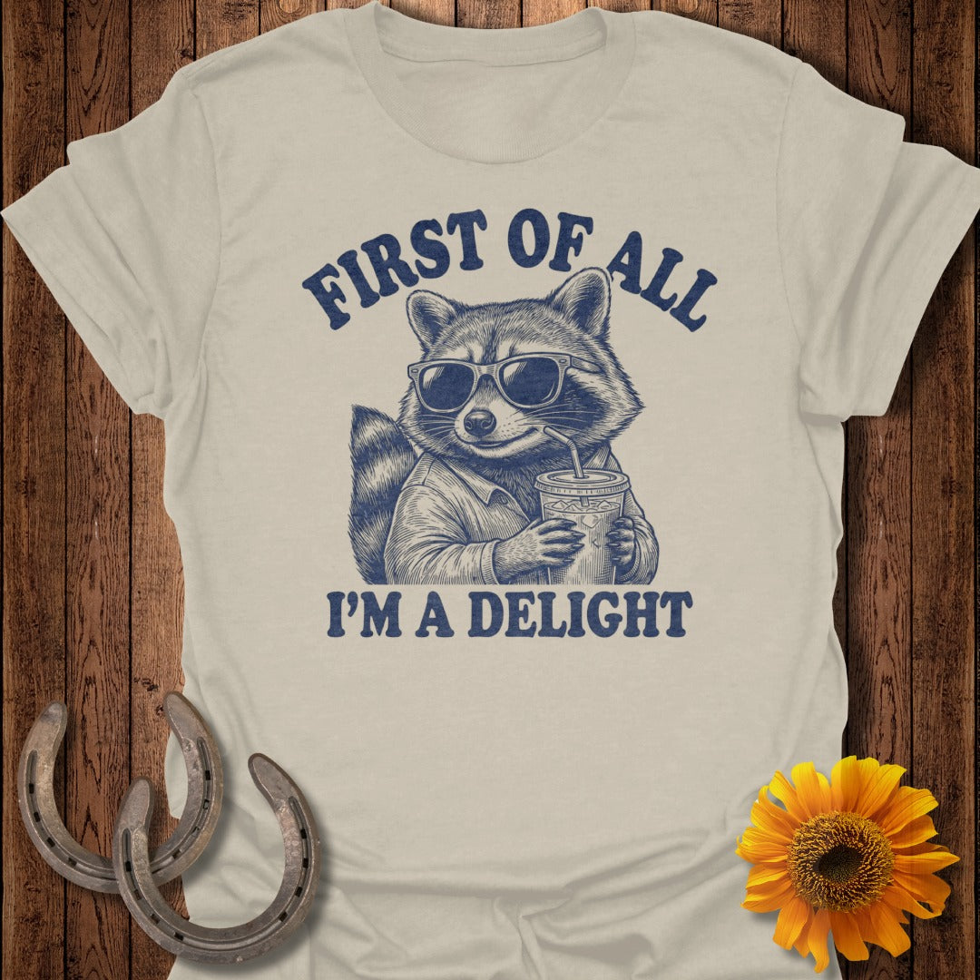 T-shirt graphic of raccoon wearing sunglasses, holding a drink, with text "FIRST OF ALL I'M A DELIGHT".