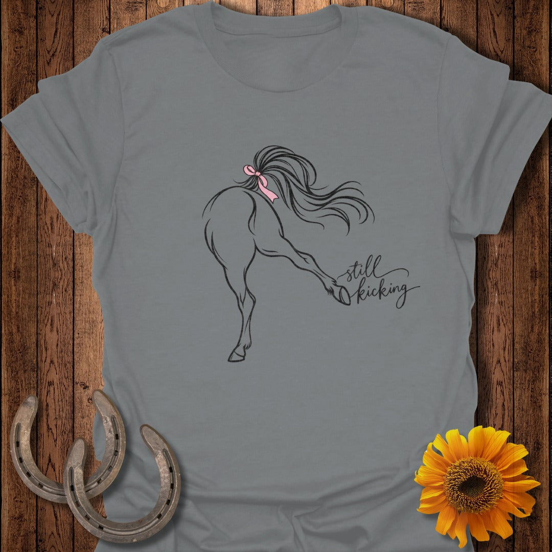 Grey t-shirt with line drawing of horse kicking, pink bow, and "still kicking" text.