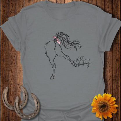 Grey t-shirt with line drawing of horse kicking, pink bow, and "still kicking" text.