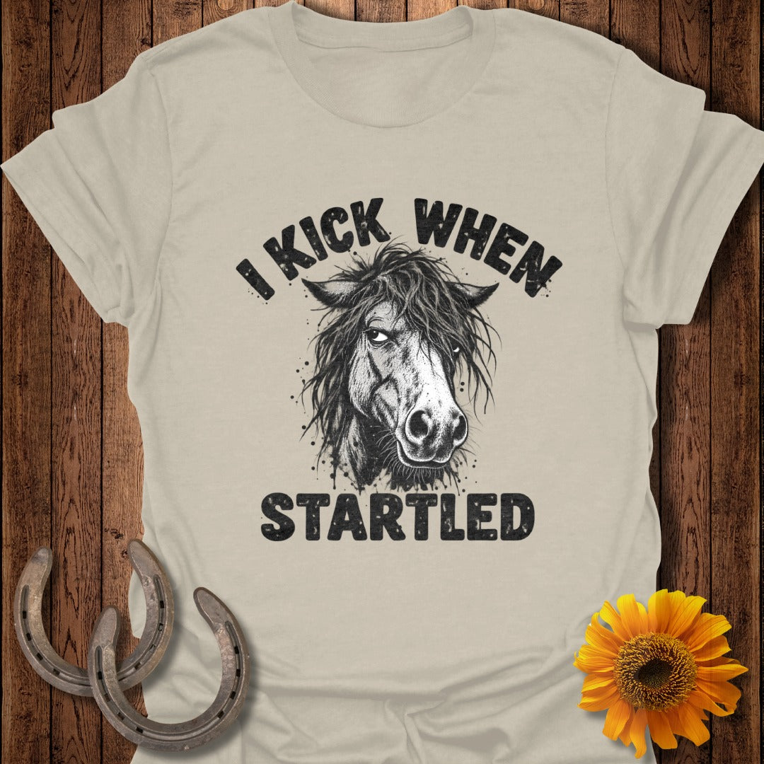 Beige t-shirt featuring a graphic of a horse head and the text "I KICK WHEN STARTLED".