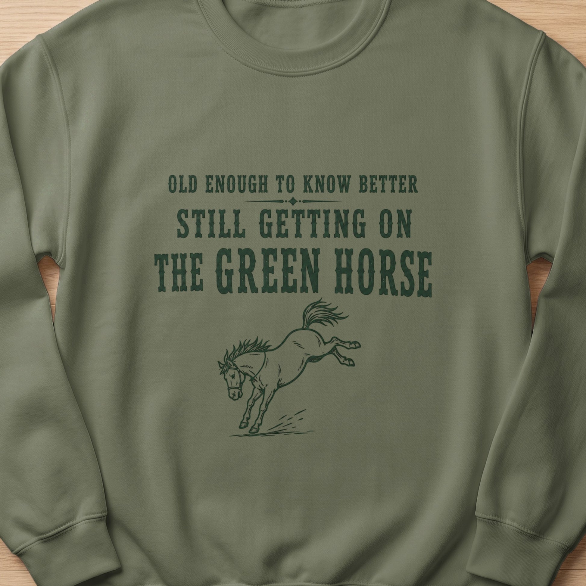 Green sweatshirt with text "OLD ENOUGH TO KNOW BETTER STILL GETTING ON THE GREEN HORSE" and a horse graphic.