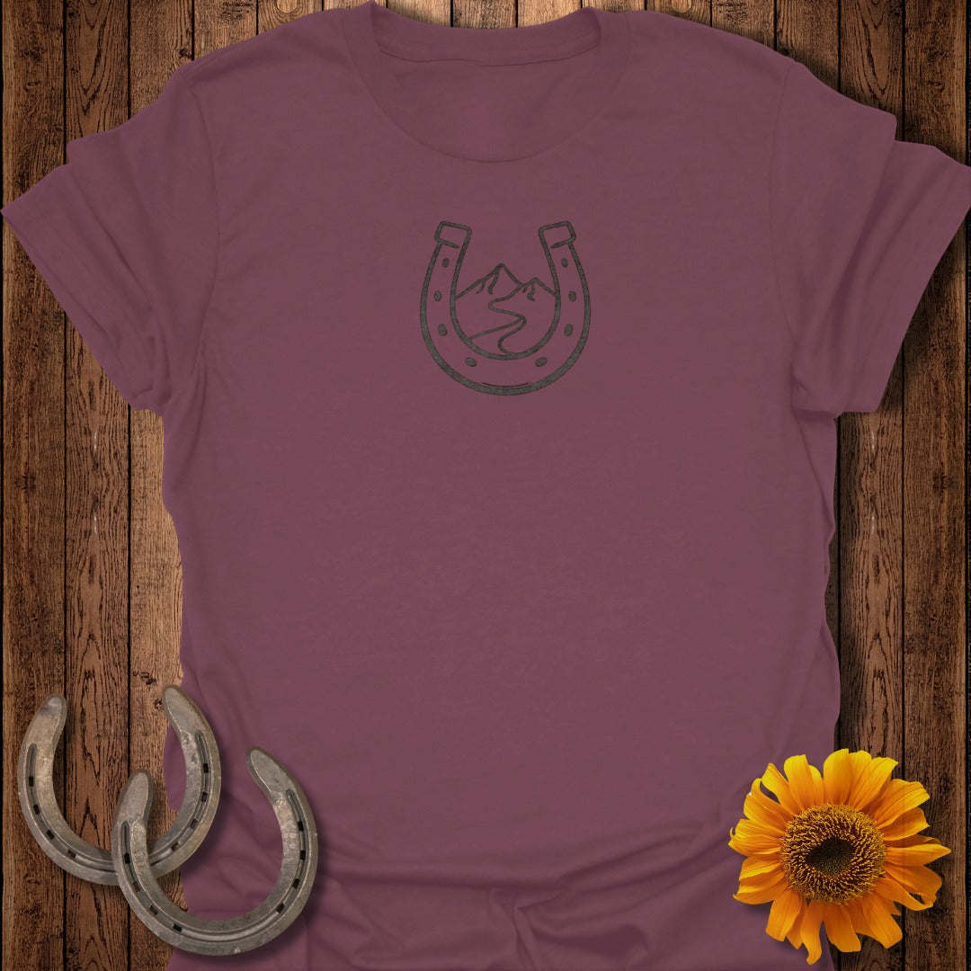 Burgundy t-shirt with horseshoe and mountain graphic on wood background.