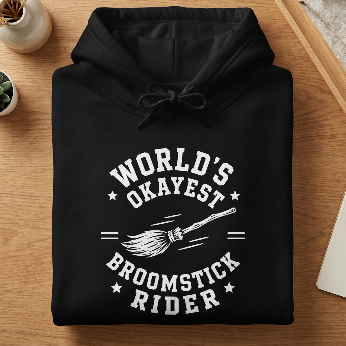 Black hoodie with white text "World's Okayest Broomstick Rider" and a broom.