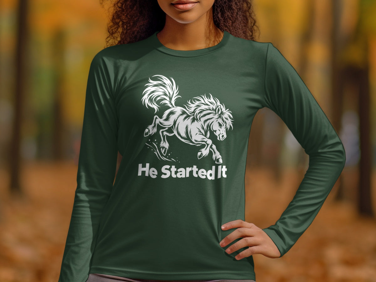 A person wearing a dark green long-sleeve shirt with a white graphic of a bucking horse and the text He Started It.