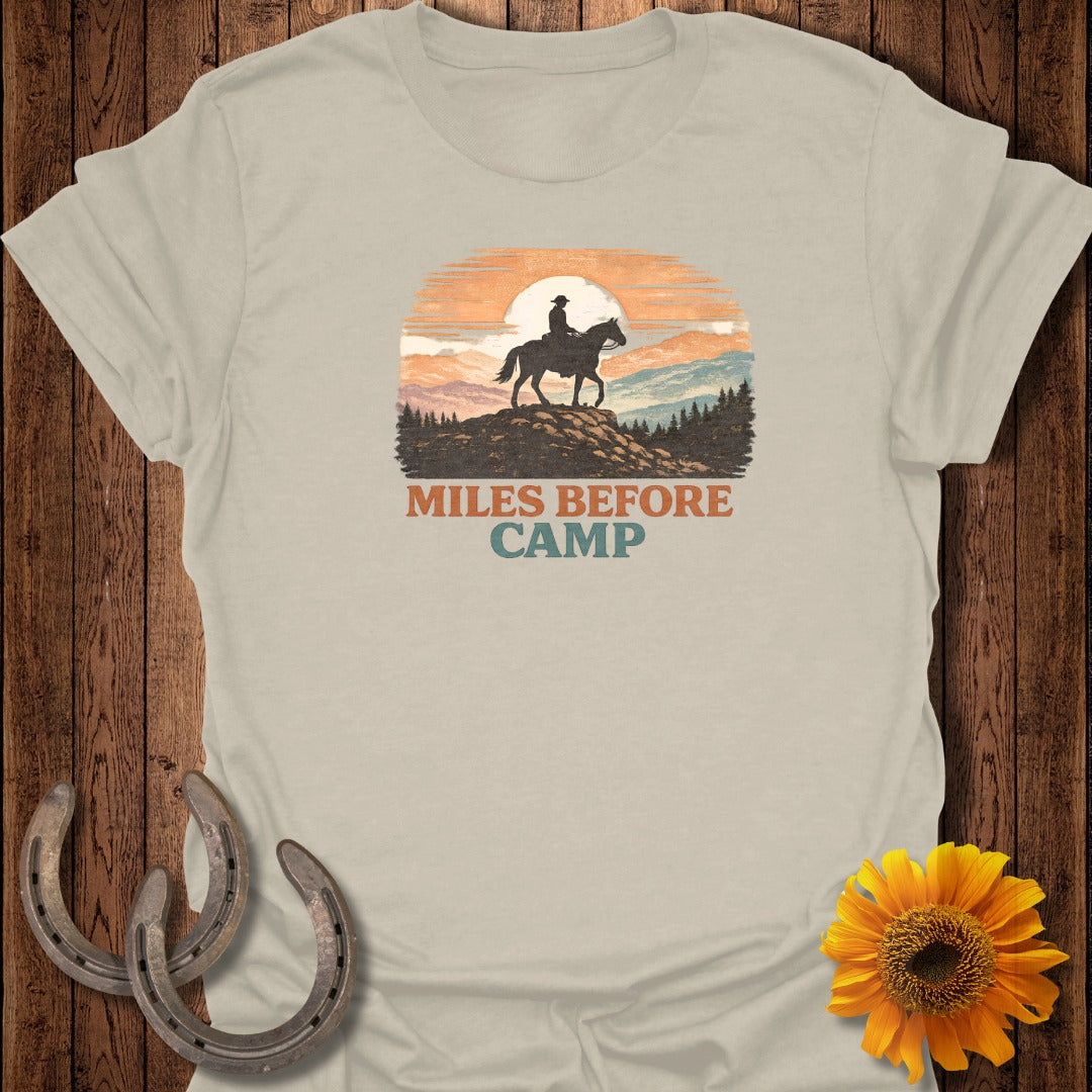 Light beige t-shirt with retro graphic of a rider on a horse and text "Miles Before Camp".