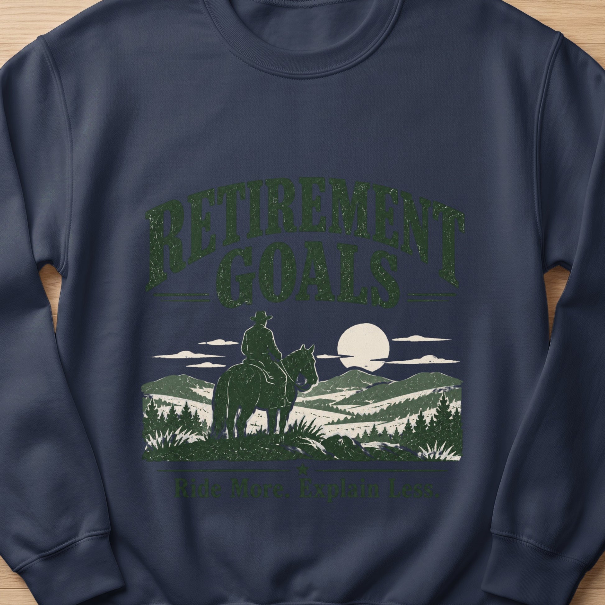 Dark blue sweatshirt with "Retirement Goals Ride More. Explain Less." text and cowboy on horse.