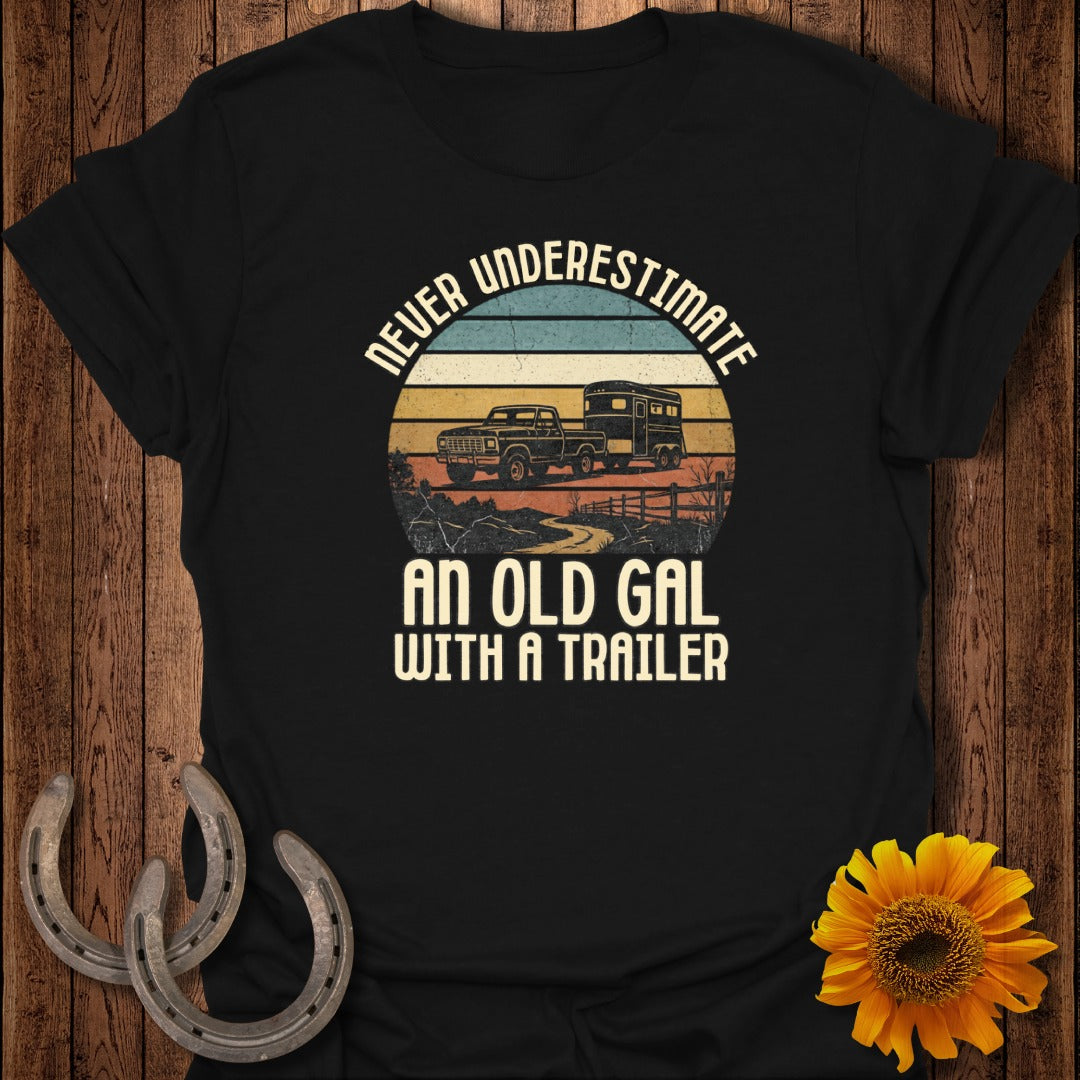 Black t-shirt with vintage truck and trailer design and text "NEVER UNDERESTIMATE AN OLD GAL WITH A TRAILER".