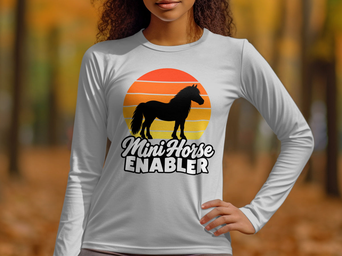 A person wearing a light gray long-sleeve shirt with a graphic of a horse and sunset.