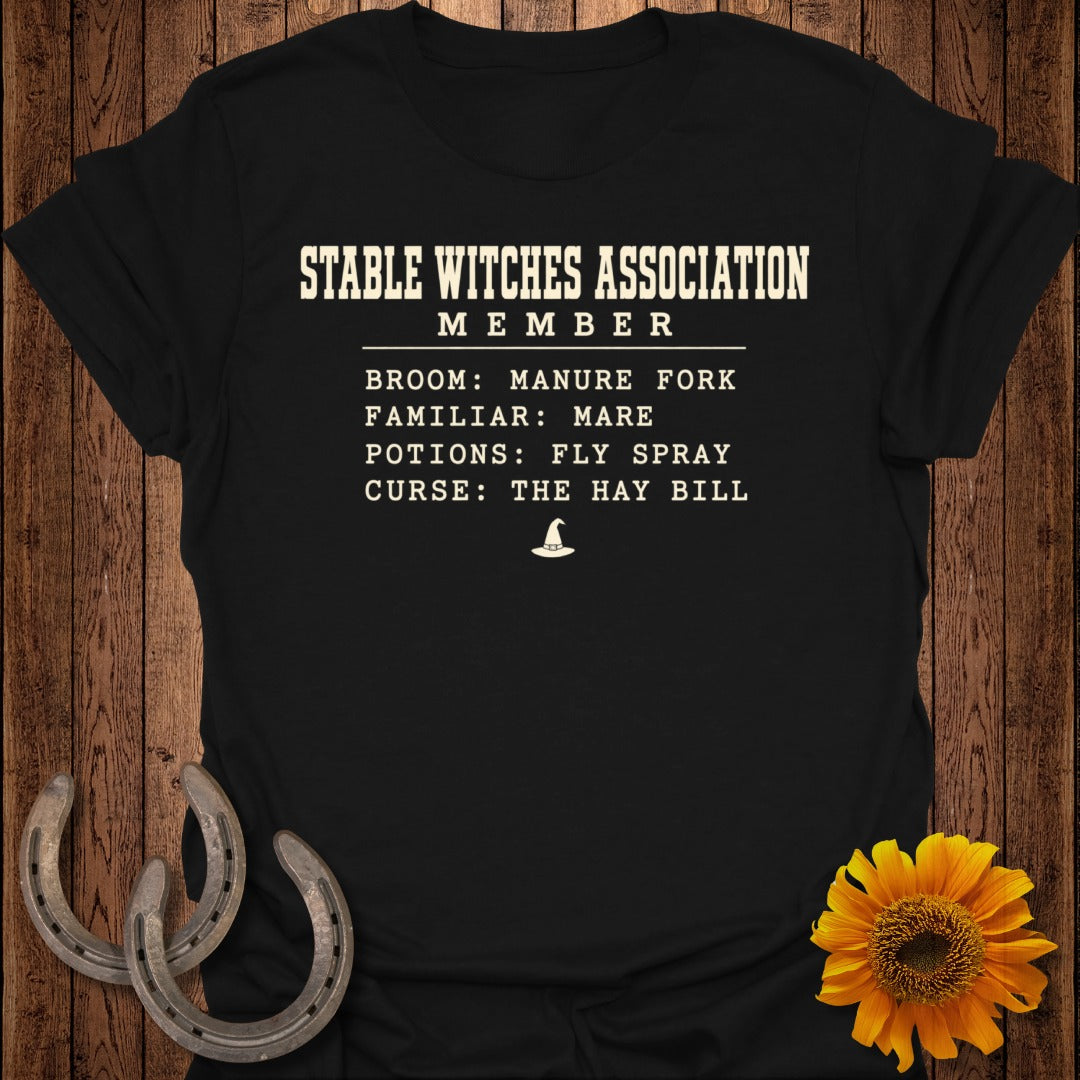 Black t-shirt with "Stable Witches Association Member" text listing broom, familiar, potions, and curse.