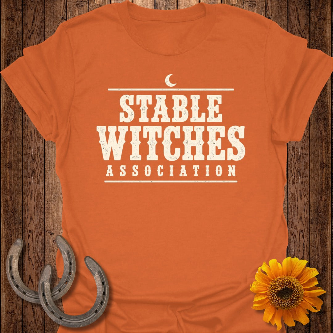 Orange t-shirt with "STABLE WITCHES ASSOCIATION" text and moon graphic.