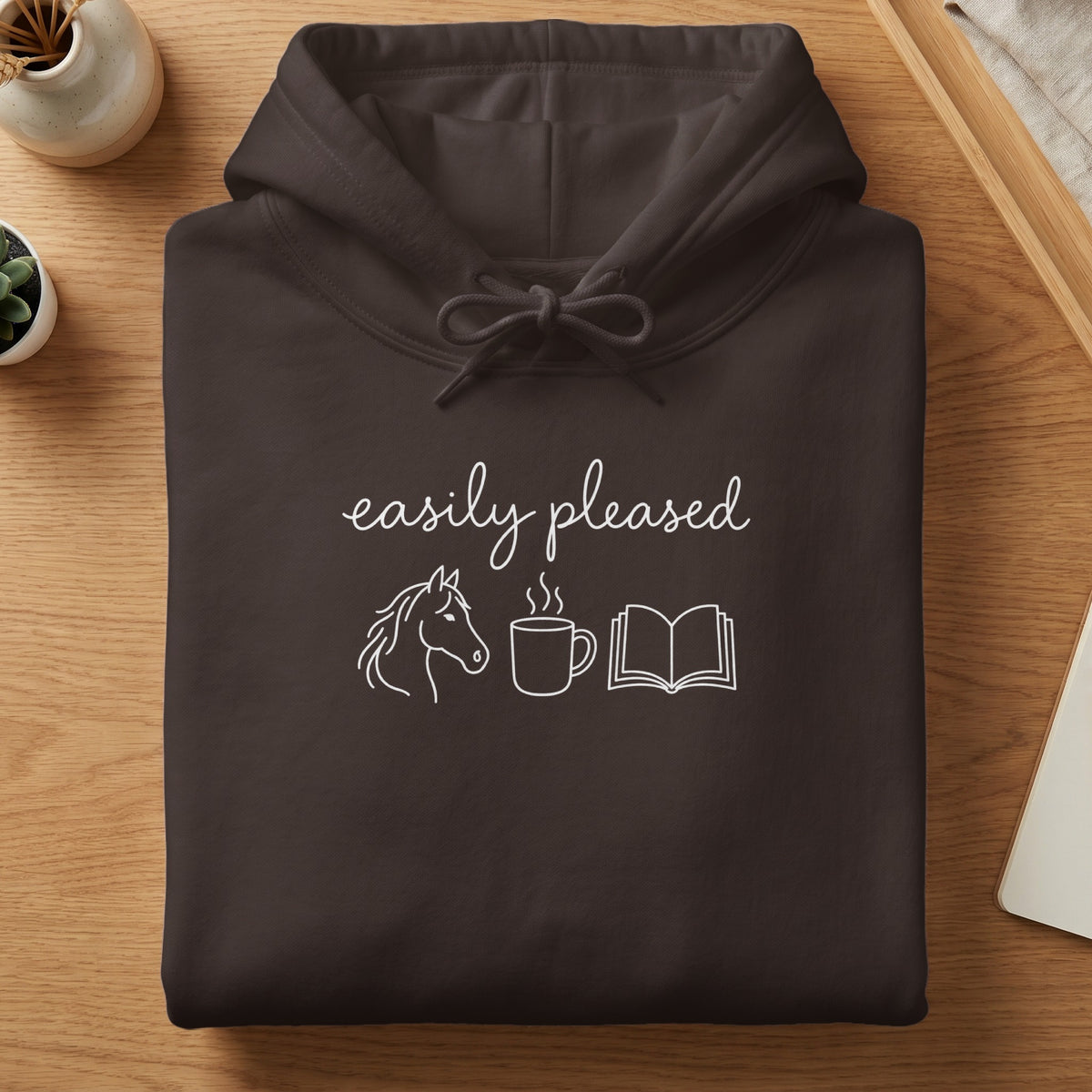 Brown hoodie with white text: "easily pleased", horse, coffee cup, and open book.
