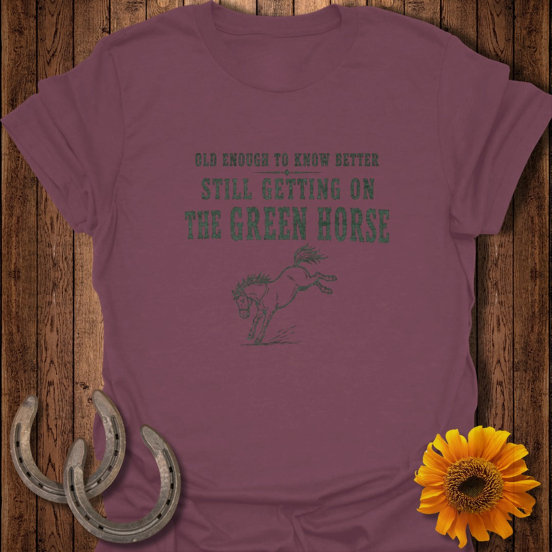 Burgundy t-shirt with green text and horse graphic: "Old enough to know better, still getting on the green horse."