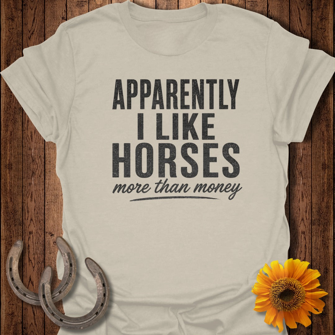 Light beige t-shirt with black text "APPARENTLY I LIKE HORSES more than money".