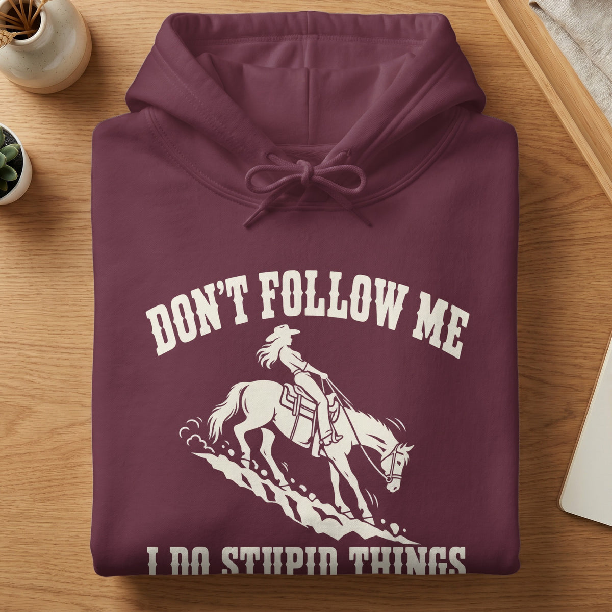 Folded maroon hoodie with white text reading "Don't Follow Me I Do Stupid Things" above a horse and rider graphic.