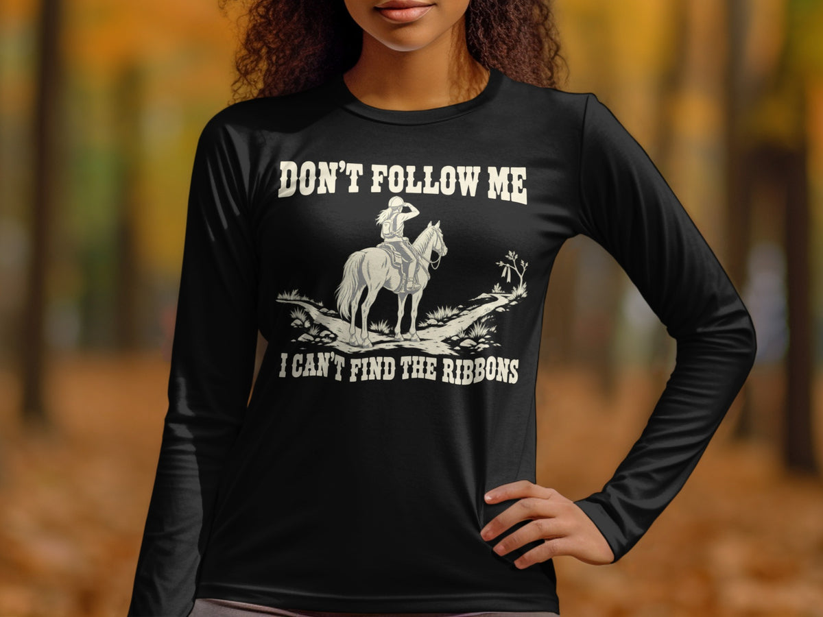 A woman wearing a long-sleeved black t-shirt printed with a graphic of an equestrian rider and the text, DON'T FOLLOW ME, I CAN'T FIND THE RIBBONS.