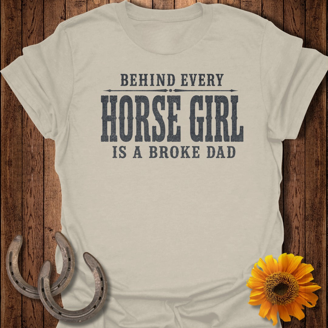 Light beige t-shirt with distressed text "BEHIND EVERY HORSE GIRL IS A BROKE DAD"