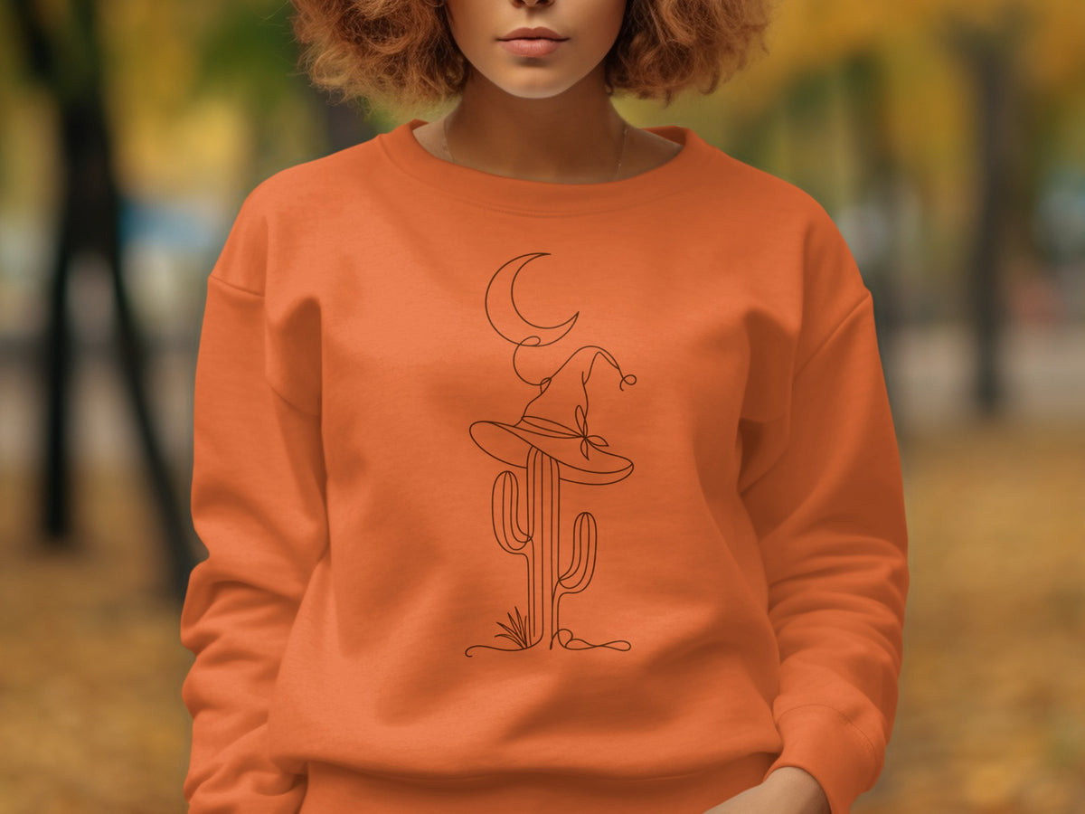 Orange sweatshirt with a line art graphic of a cactus wearing a witch hat and a crescent moon.
