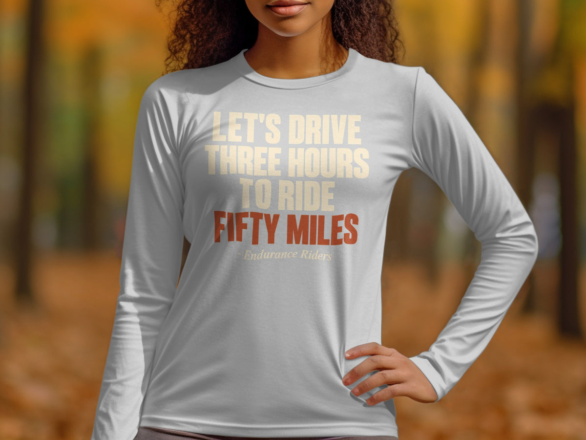 A person wearing a long-sleeved gray shirt printed with the text LET'S DRIVE THREE HOURS TO RIDE FIFTY MILES.