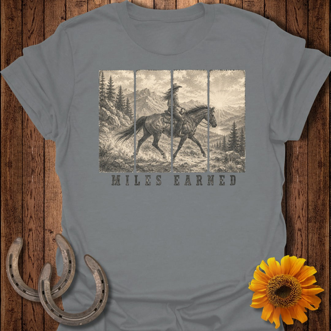 Grey t-shirt with vintage cowboy on horseback graphic and "MILES EARNED" text.