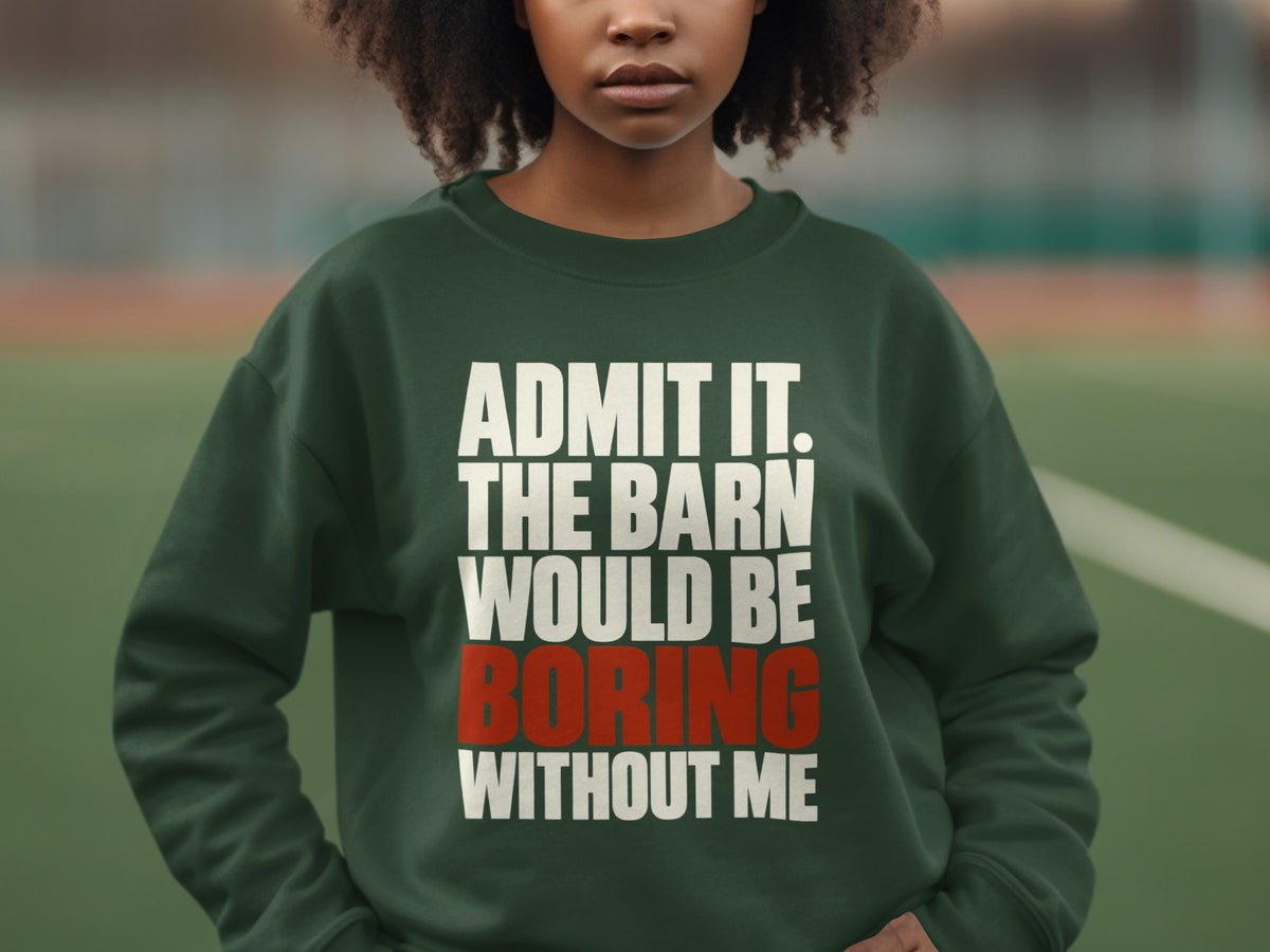 A person wearing a dark green crewneck sweatshirt featuring white and red text reading ADMIT IT. THE BARN WOULD BE BORING WITHOUT ME.