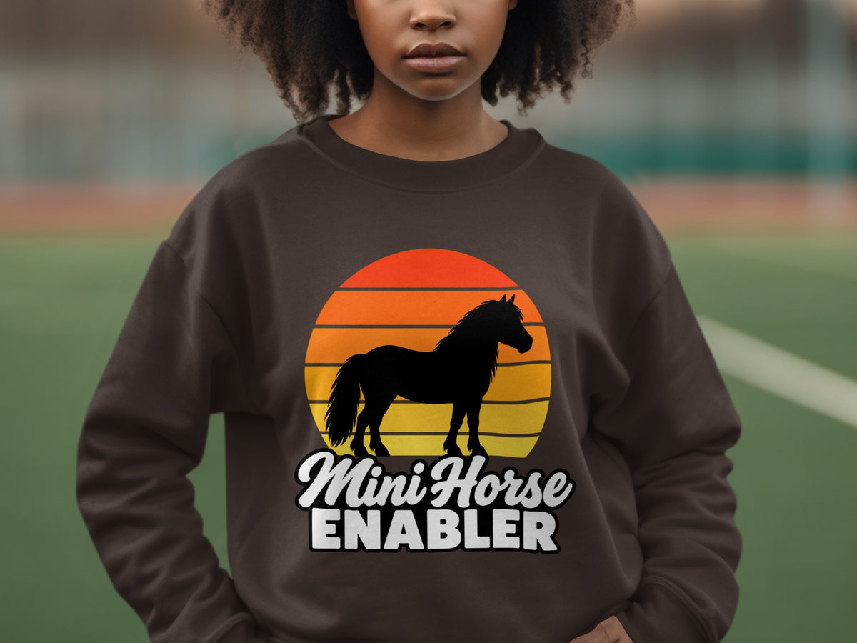 A brown crewneck sweatshirt featuring a black horse silhouette over a colorful sunset graphic and the text Mini Horse Enabler.