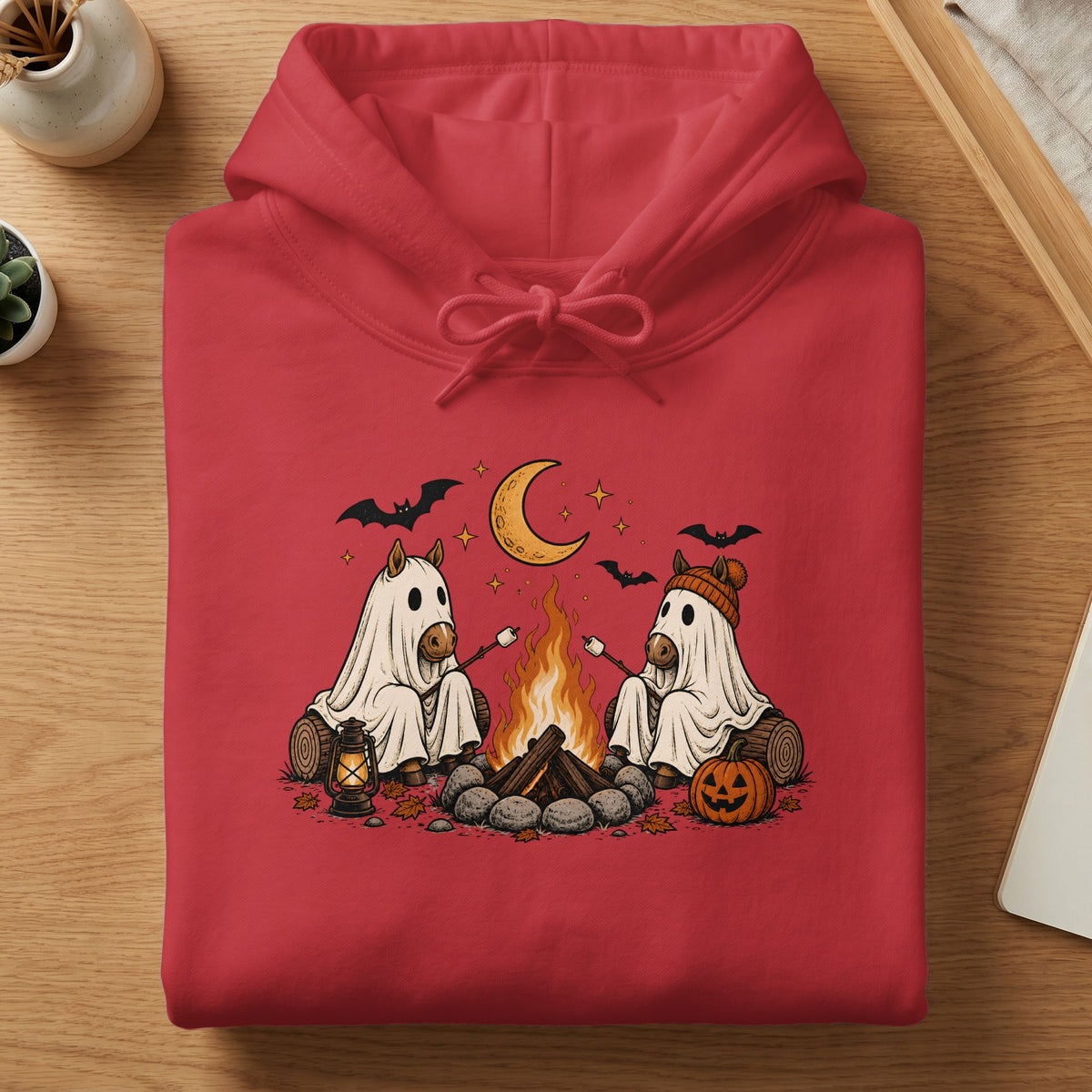 Two horses in ghost costumes roast marshmallows by a campfire under a crescent moon.